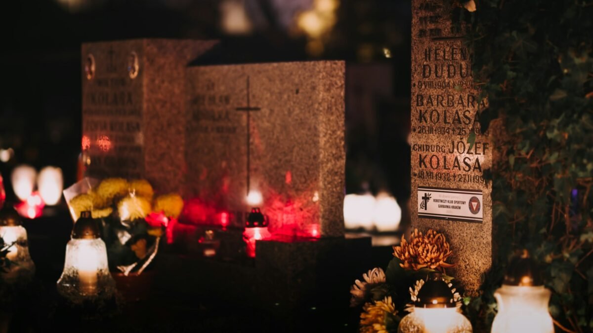 Candles and flowers glowing beside grave markers at night, a scene of All Souls' Day remembrance